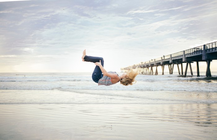 Woman doing a backflip on a beach with a pier