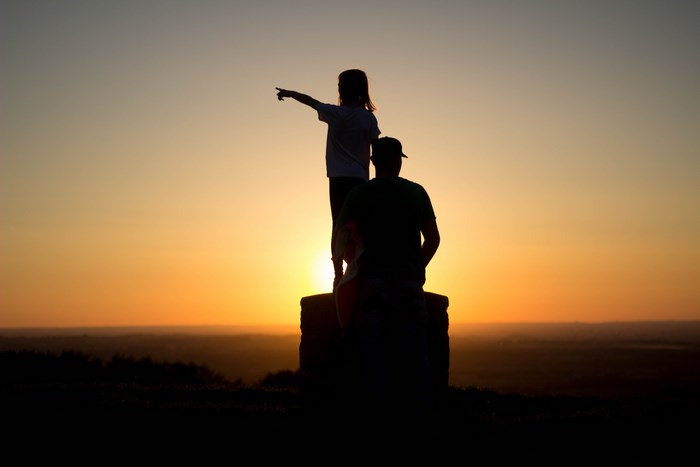 Silhouette of a girl pointing with a man behind her at sunset