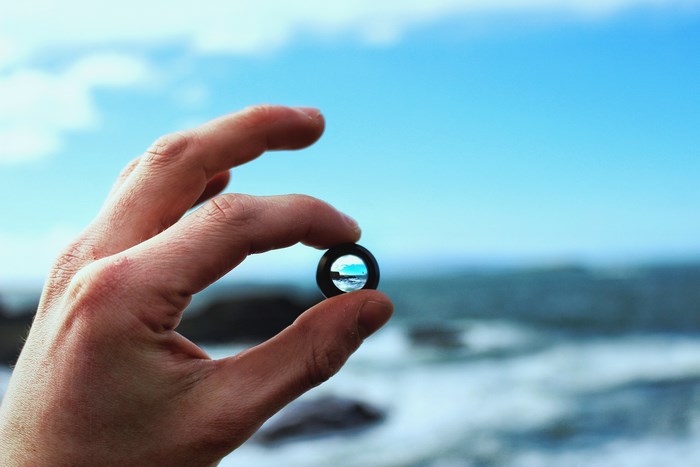 Hand holding a lens with ocean and sky view