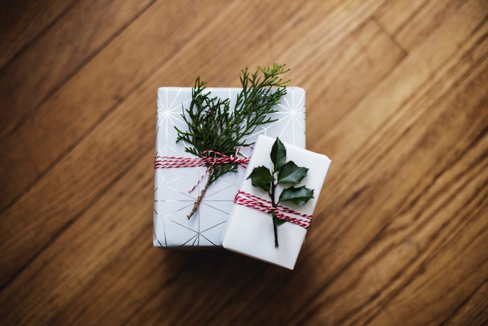 Two Christmas gifts with natural foliage on wooden surface