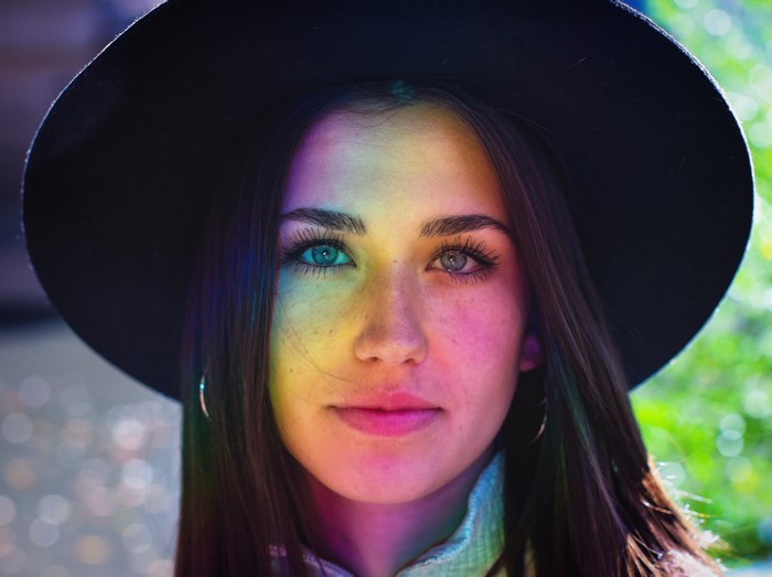 Woman wearing a hat with rainbow light on her face