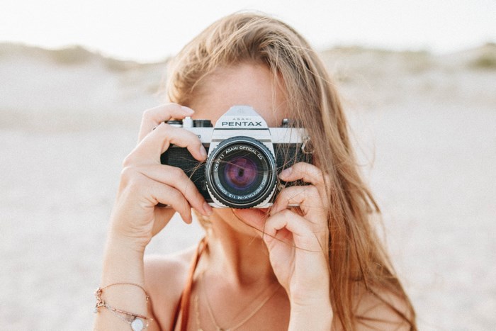 Woman holding a Pentax K1000 camera on a beach