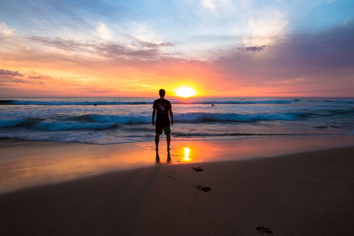 Man standing on beach at sunset with ocean waves