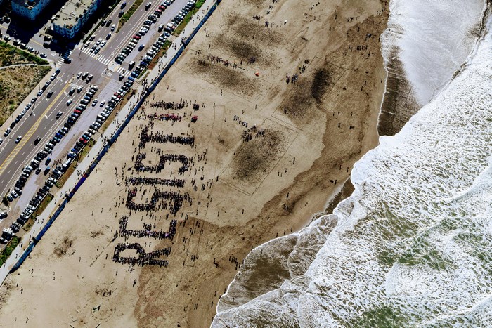 Aerial view of a crowd forming the word RESIST on a beach