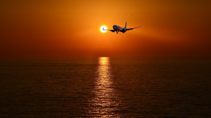 Airplane flying over the ocean at sunset