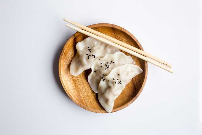 Dumplings with sesame seeds on a wooden plate with chopsticks