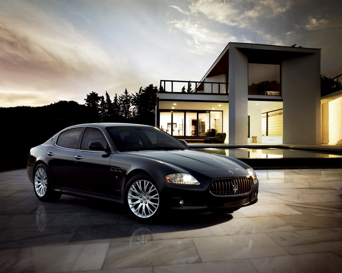 Black Maserati Quattroporte parked by a modern house at dusk