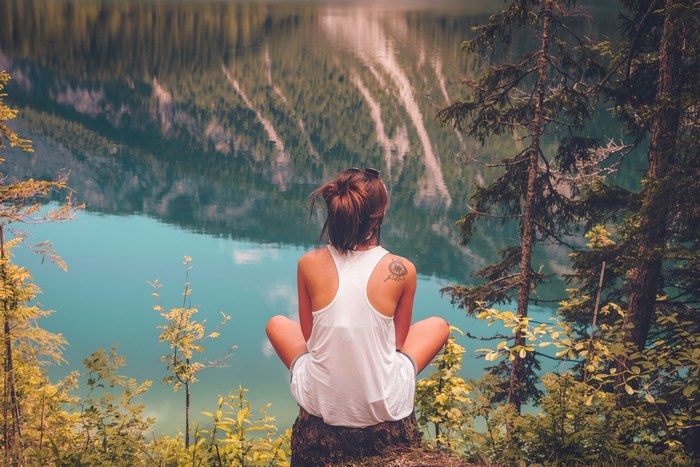 Woman sitting by a lake with mountain reflection