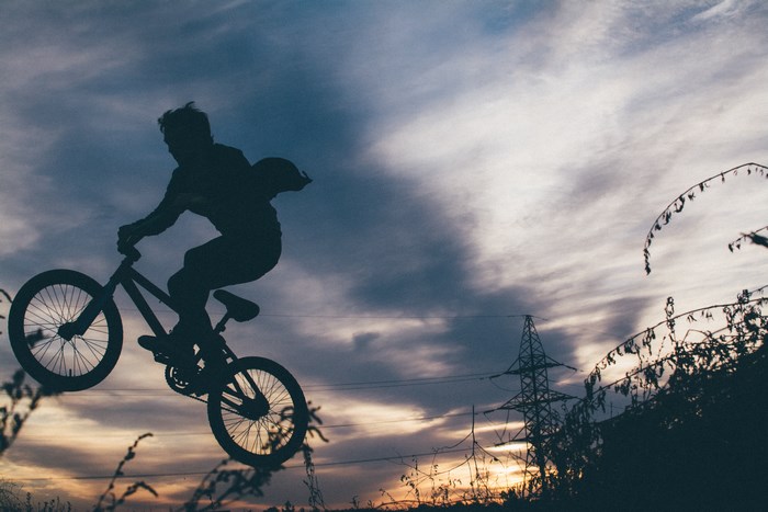 Silhouette of a BMX rider jumping against a cloudy sky