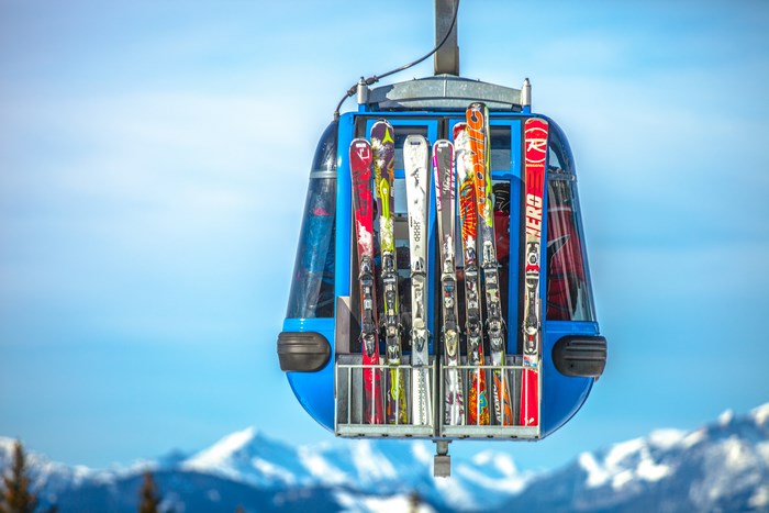 Blue ski lift gondola carrying skis up a snowy mountain
