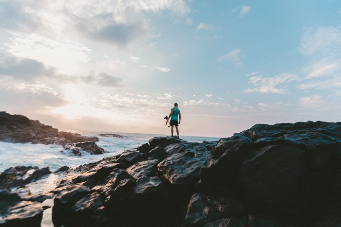 Man with camera standing on rocks by the sea