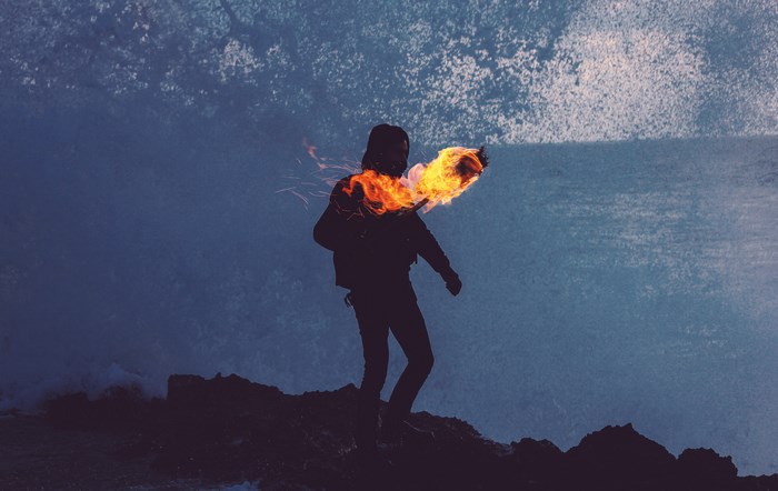 Person holding a torch on a rocky shore with waves