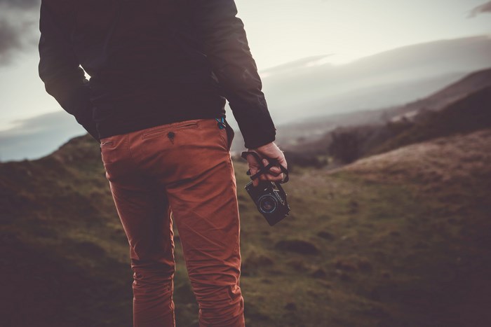 Man holding a Pentax camera in the hills at sunset