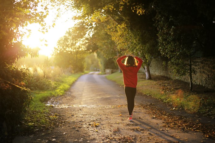 Woman in red hoodie walking on a country road at sunset