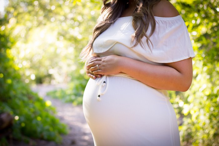 Pregnant woman in white dress holding her belly