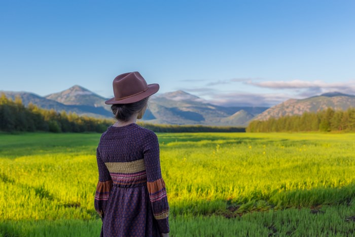 Woman in a hat and dress in a field with mountains