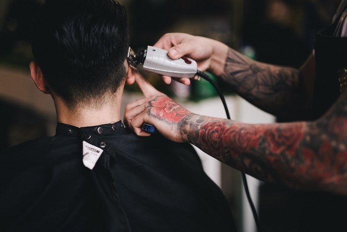 Barber with tattooed arms cuts a man's hair