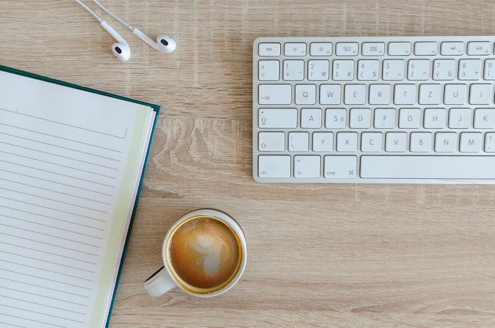 Flatlay of a keyboard, notebook, earphones, and coffee on a wooden desk
