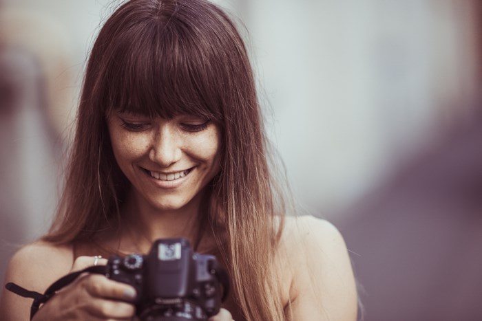 Woman with bangs holding a camera and smiling