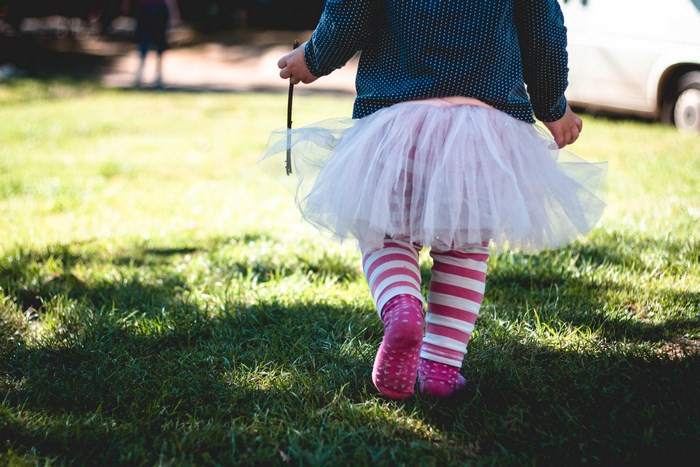 Child in tutu and striped socks walking on grass