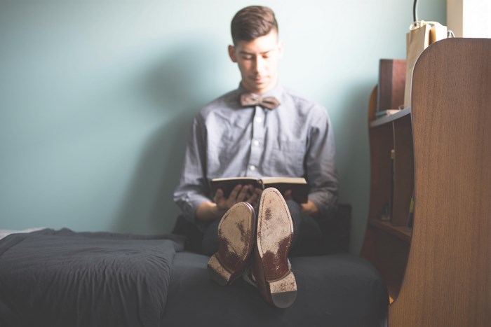 Man in bow tie reading a book on a bed