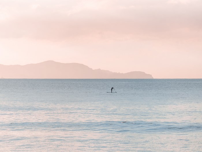 Person paddleboarding on the ocean with mountains in the background