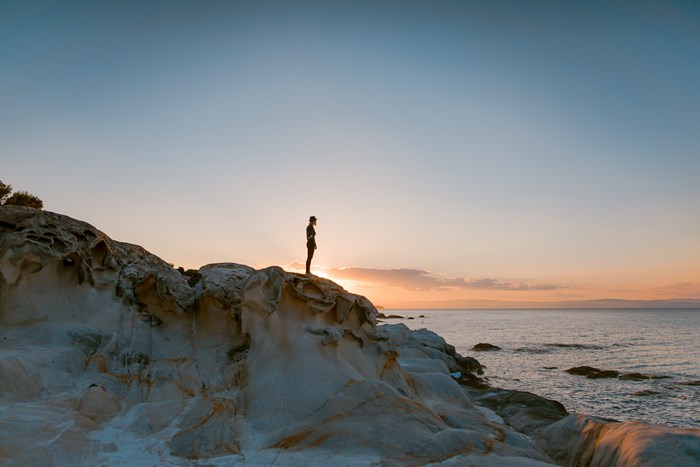 Woman on a rocky coast at sunset in Greece