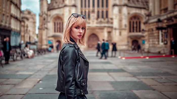 Woman in leather jacket with sunglasses in front of building