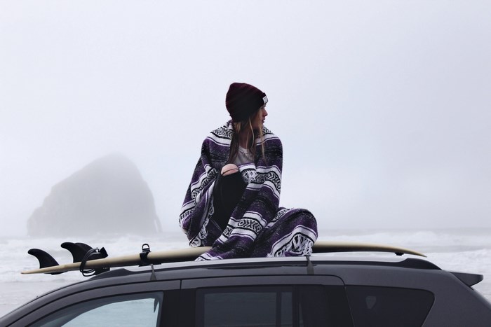 Woman in blanket on car roof with surfboard