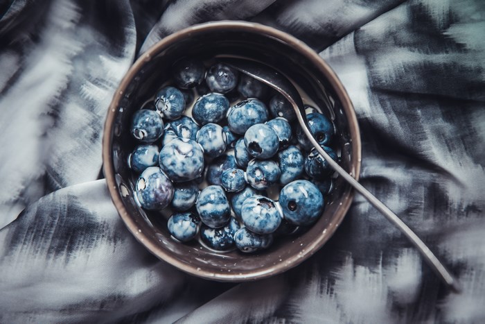 Bowl of blueberries with cream and spoon on fabric