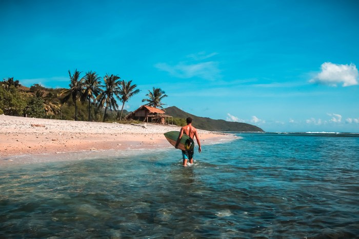 Man with surfboard walks into the ocean in Indonesia