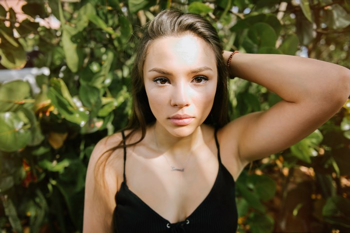 Woman with hand in hair in front of foliage