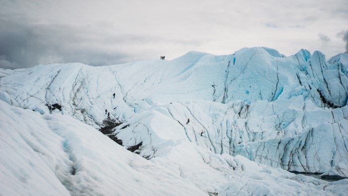 People climbing on a vast blue glacier under a cloudy sky