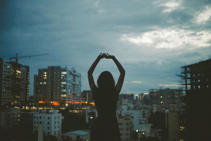 Silhouette of a woman with arms raised against city skyline