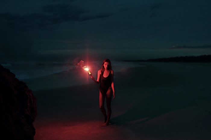 Woman holding a red flare on a beach at twilight
