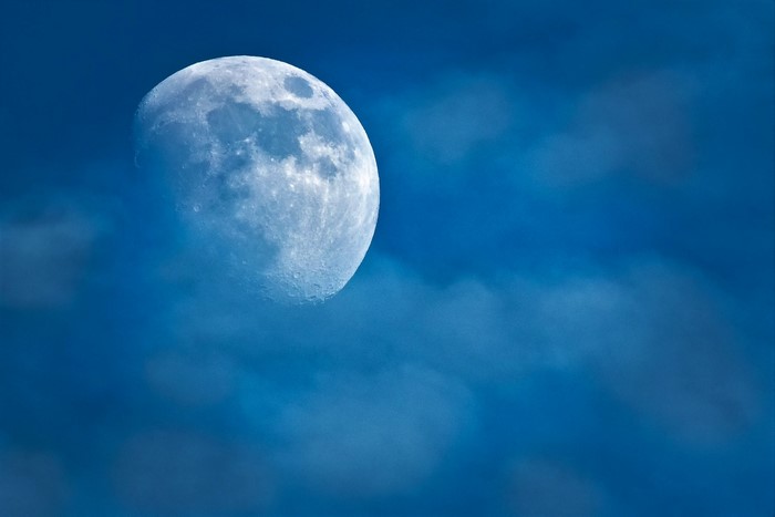 Moon partially obscured by clouds in a blue sky