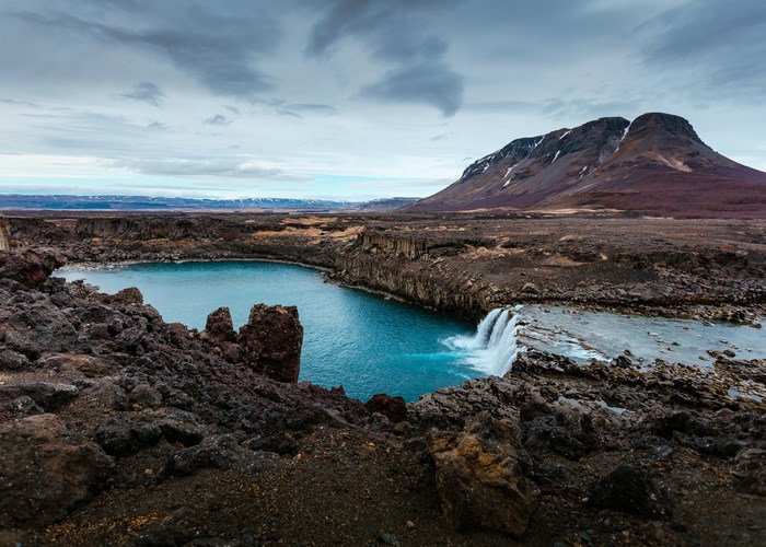 Blue lake and waterfall in Iceland with a mountain