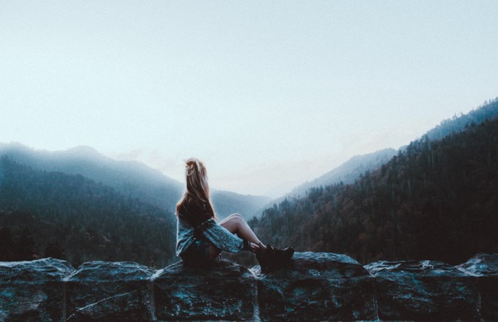Woman sitting on a stone wall overlooking misty mountains