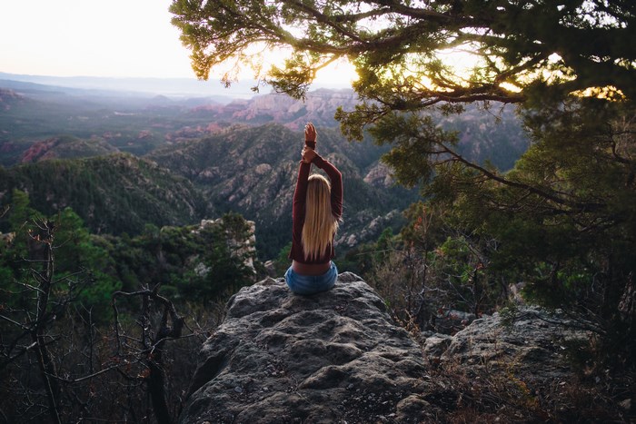 Woman meditating on a cliff edge at golden hour