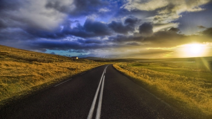 Road through a grassy landscape under a dramatic sky