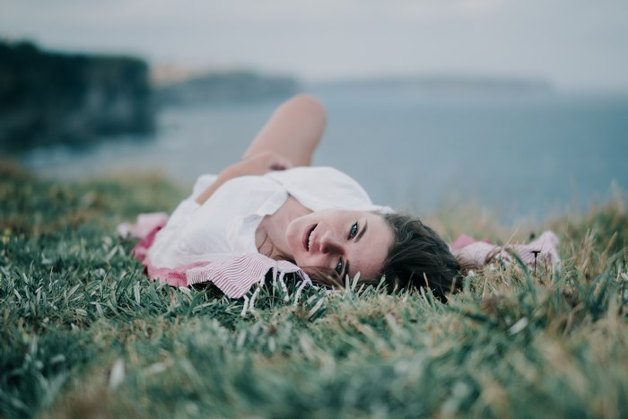Woman in white shirt lying on grass by the water