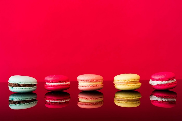 Five colorful macarons on a reflective surface
