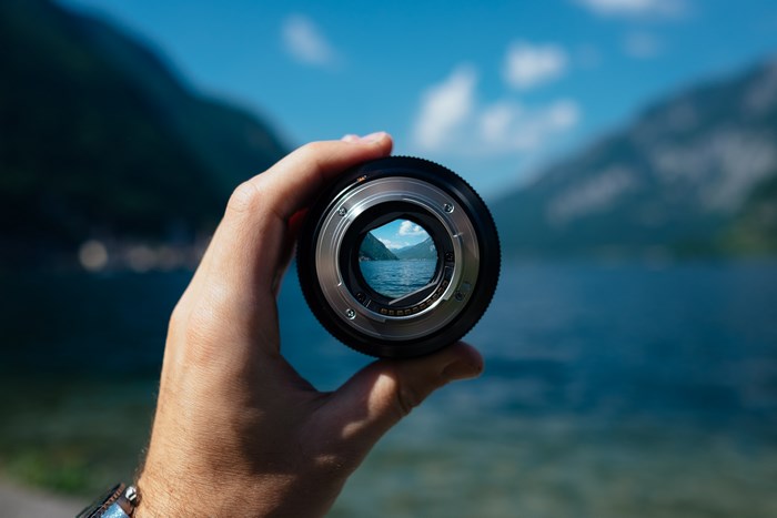 Hand holding camera lens with lake and mountains view