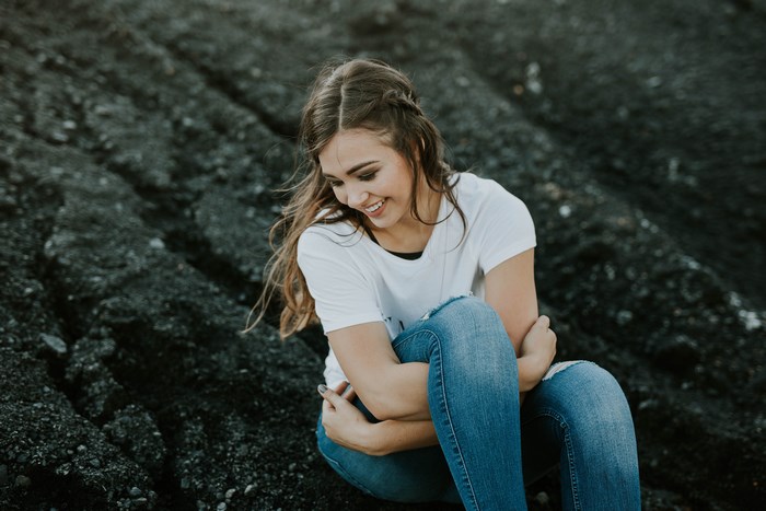 Young woman in ripped jeans sitting on dark rocks