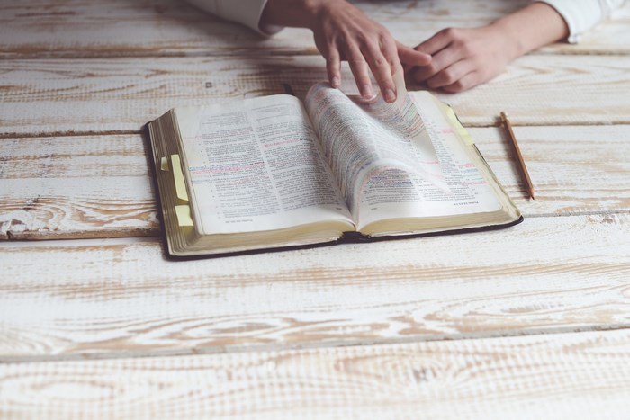 Hands turning pages of a bible with sticky notes