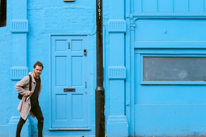 Man with beard and backpack in front of blue door in London
