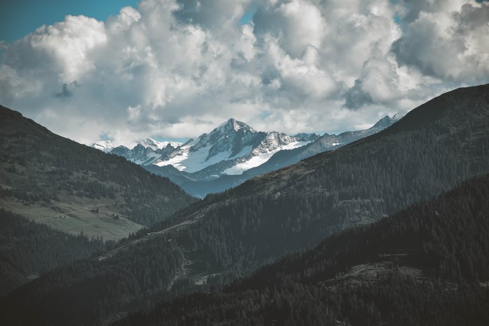 Snow-capped mountains and forested slopes under a cloudy sky