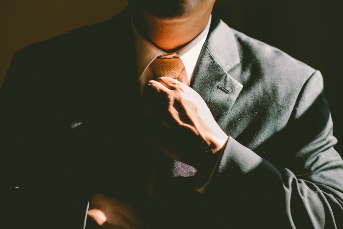 Man in a gray suit adjusting his yellow tie