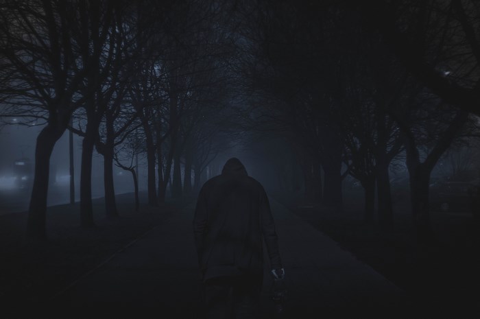 Person in hoodie walking on a dark, foggy path