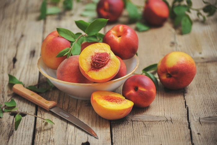 Peaches in a bowl with a knife on a wooden table
